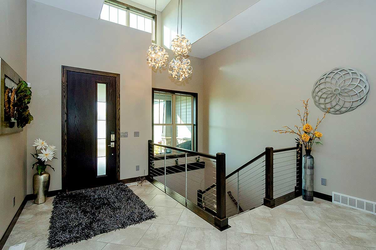 Interior foyer with dark wood front door, vaulted ceiling, modern chandelier, and cable-rail staircase.