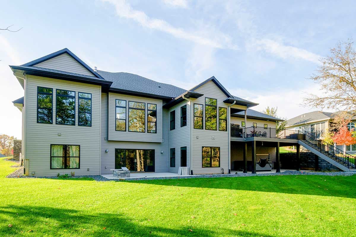 House plan exterior: Modern style, two stories, featuring a large deck with stairs, expansive windows, and gabled rooflines.