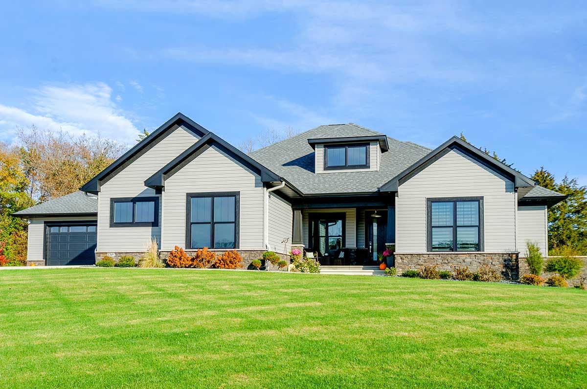 House plan exterior. Two-story home with gabled roof, dormer, and attached garage. Stone veneer accent and covered entry porch.
