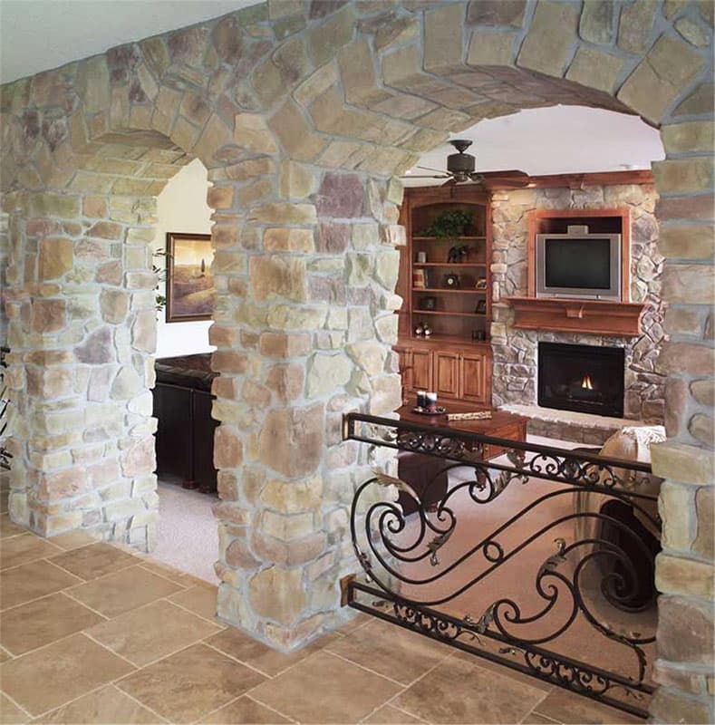 Interior view of a living room featuring stone archways, fireplace with built-in shelving, and decorative metal railing.