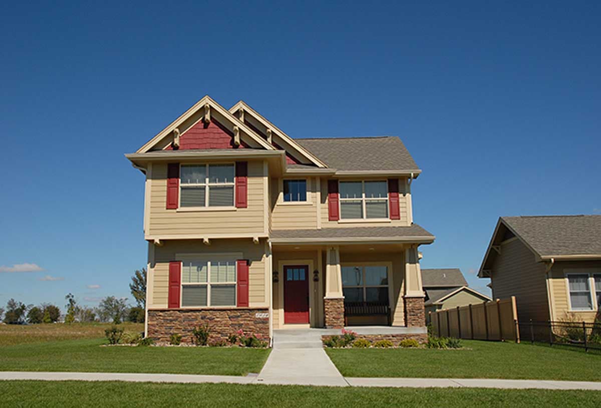 Two-story house plan exterior with gabled dormers, stone base, covered porch with bench, and red front door.