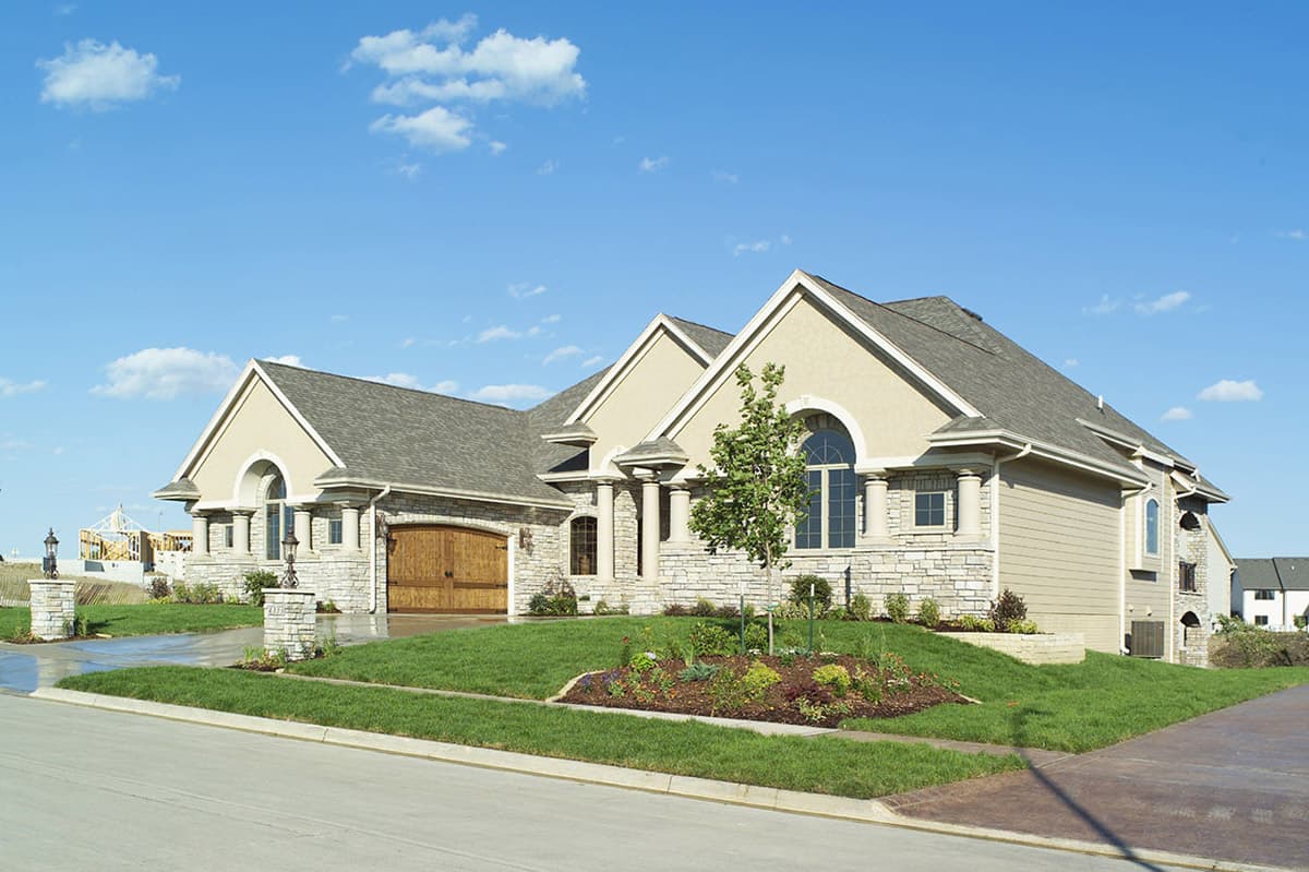 House plan exterior with stone and stucco facade, arched windows, and a three-car garage with wood doors.
