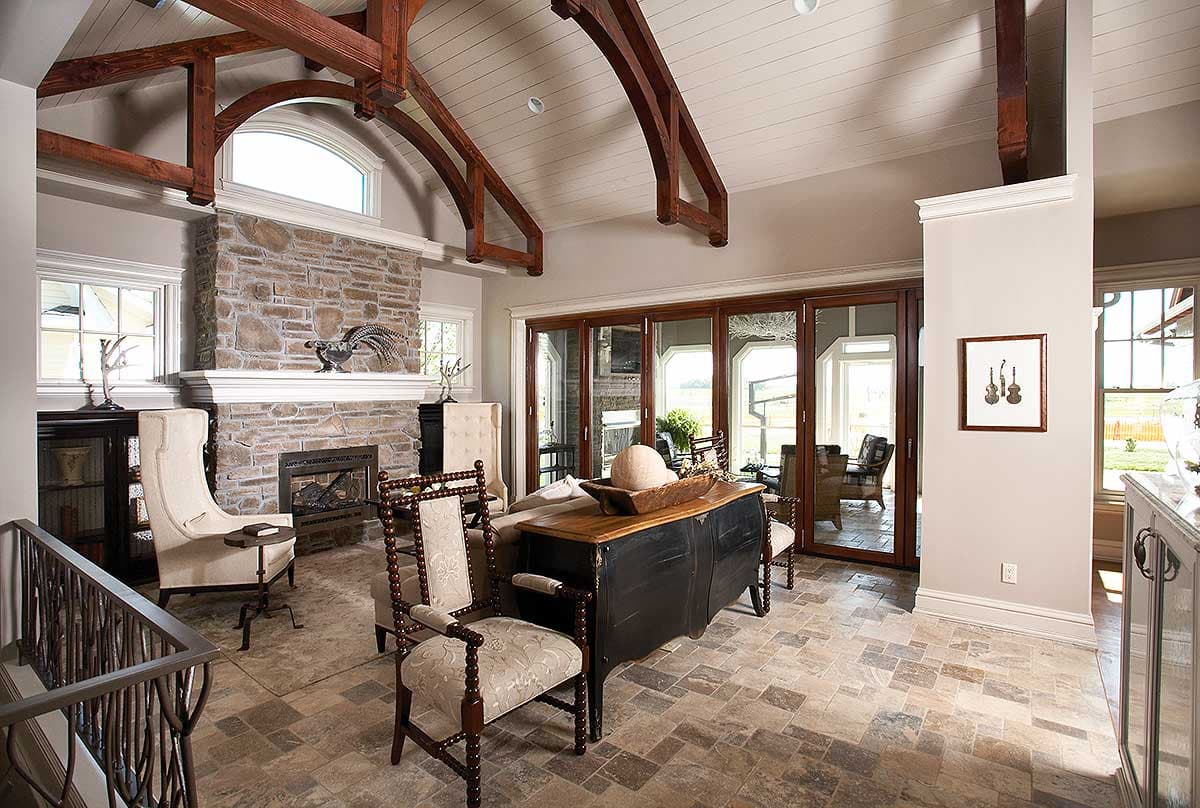 Great room with vaulted ceiling featuring exposed wood beams, stone fireplace, and folding glass doors leading to an outdoor area.