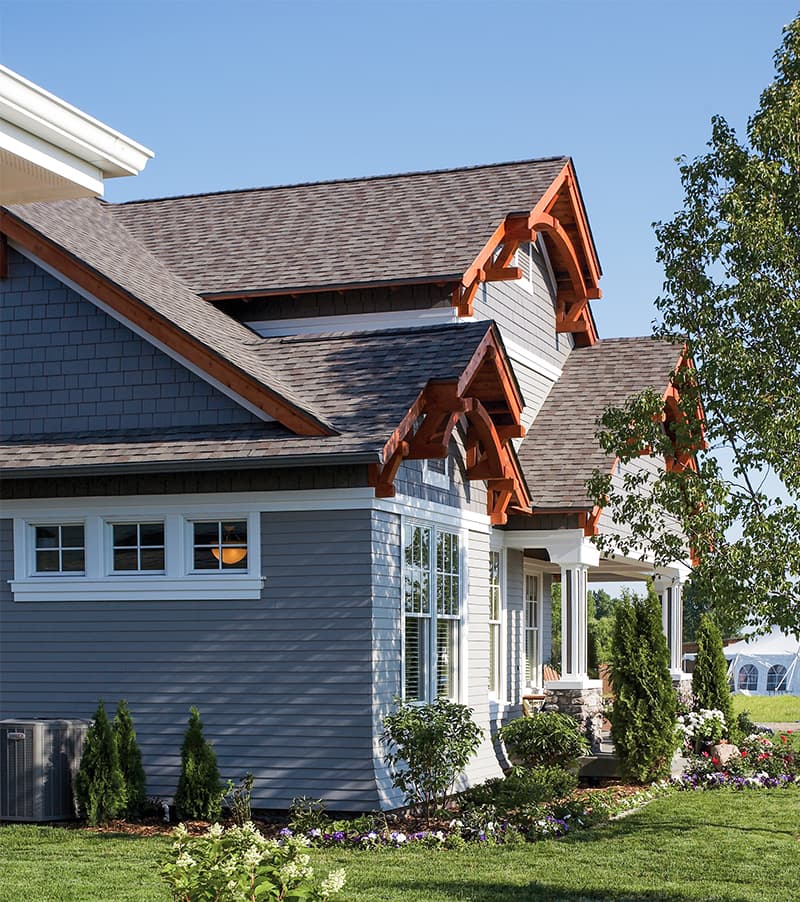 House plan exterior with a shingled facade, exposed rafter tails, and a covered porch with stone accents.