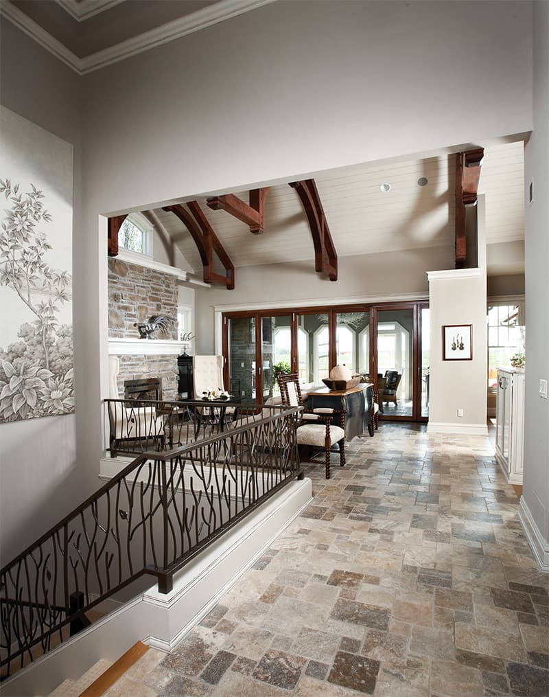 Interior view showing a great room with stone fireplace, exposed wooden beams, and large folding glass doors.