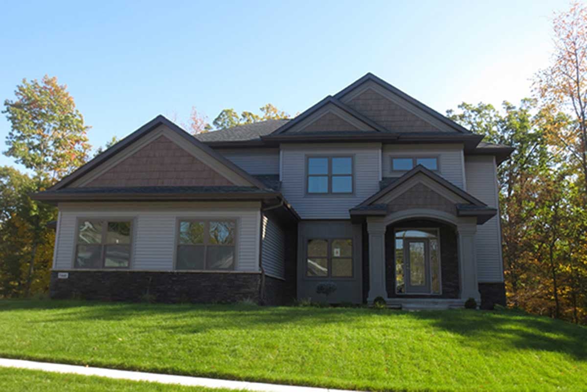 House plan exterior of two-story home with gabled dormers, stone foundation, and arched entry porch.