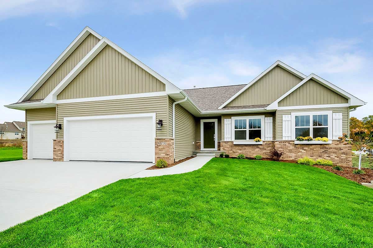 House plan exterior with two-car garage, multiple gables, vertical siding, and a brick facade at the base of the windows.