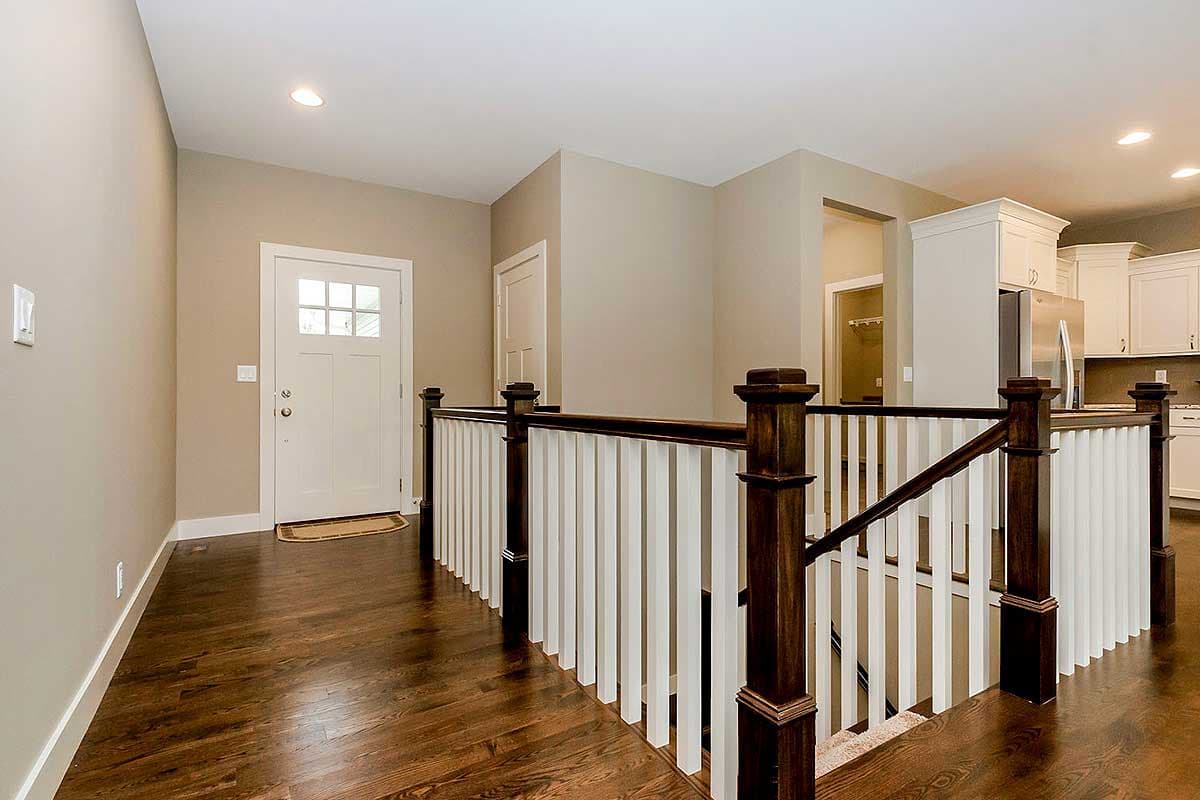 Interior view showing entrance hall with white door, dark wood floor, and railing with white spindles.