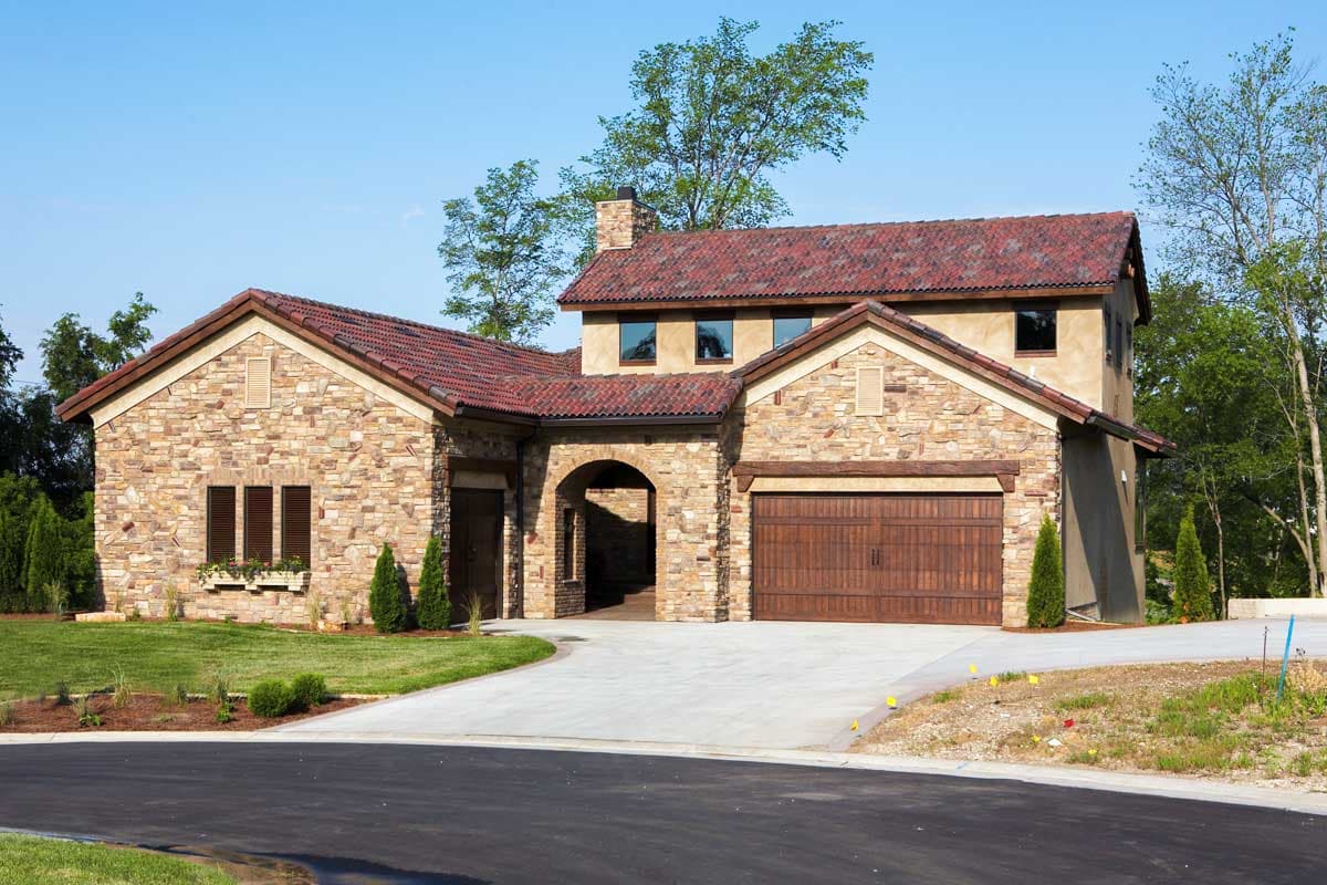 House plan exterior with stone facade, arched entryway, tiled roof, and a two-car garage.