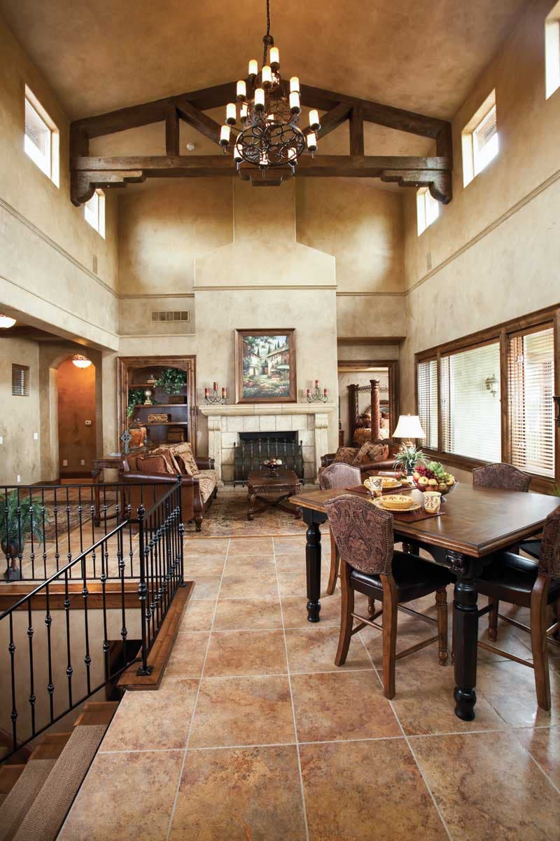 Interior view of great room with vaulted ceiling, exposed beams, stone fireplace, dining table, and staircase.