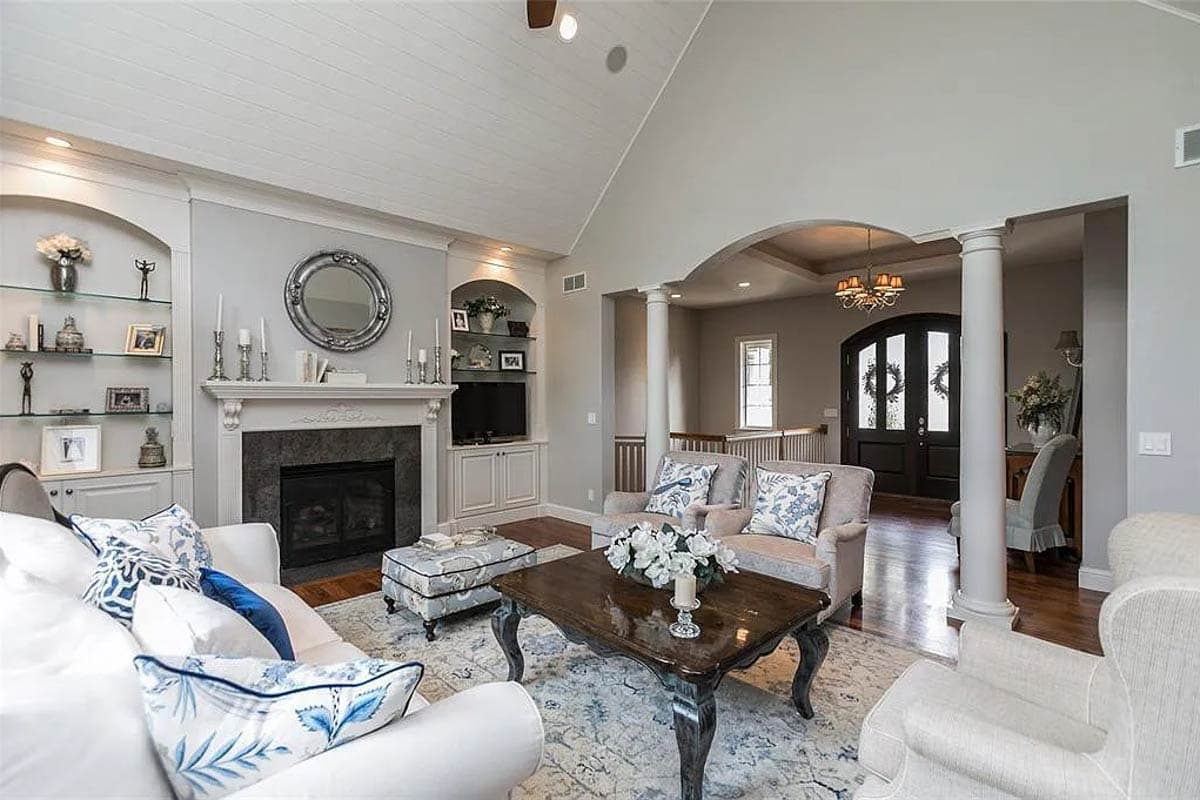 Great room with vaulted plank ceiling, fireplace, built-in shelving, and arched entryway to foyer.