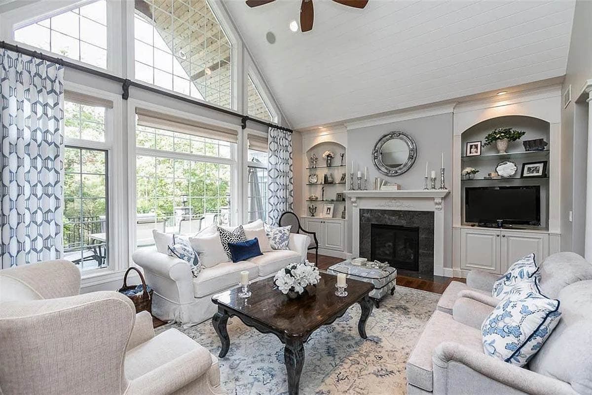 Living room with vaulted ceiling, fireplace, built-in entertainment center, and large windows with decorative curtains.