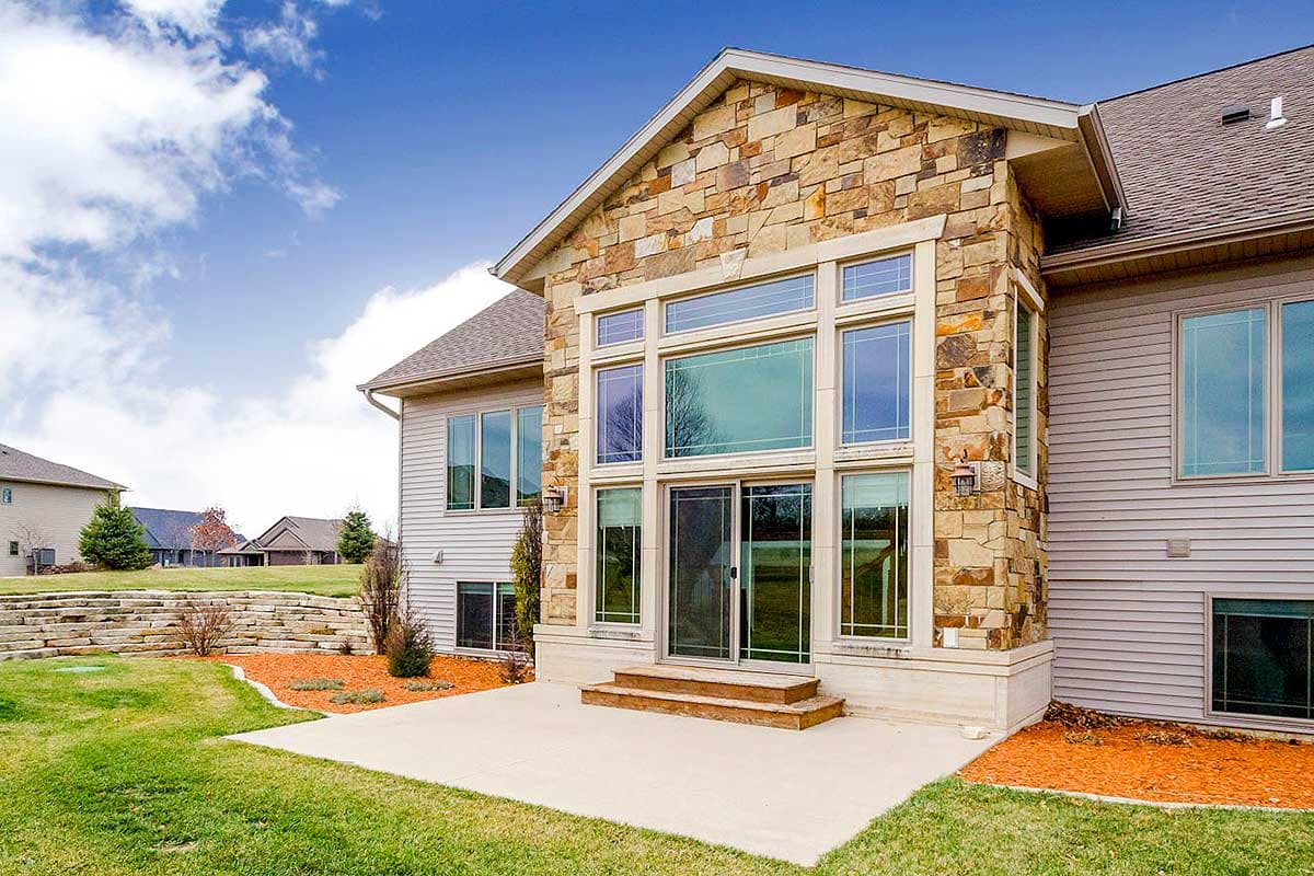 House plan exterior with layered stone facade, a wall of windows, and vinyl siding. Two stories visible.