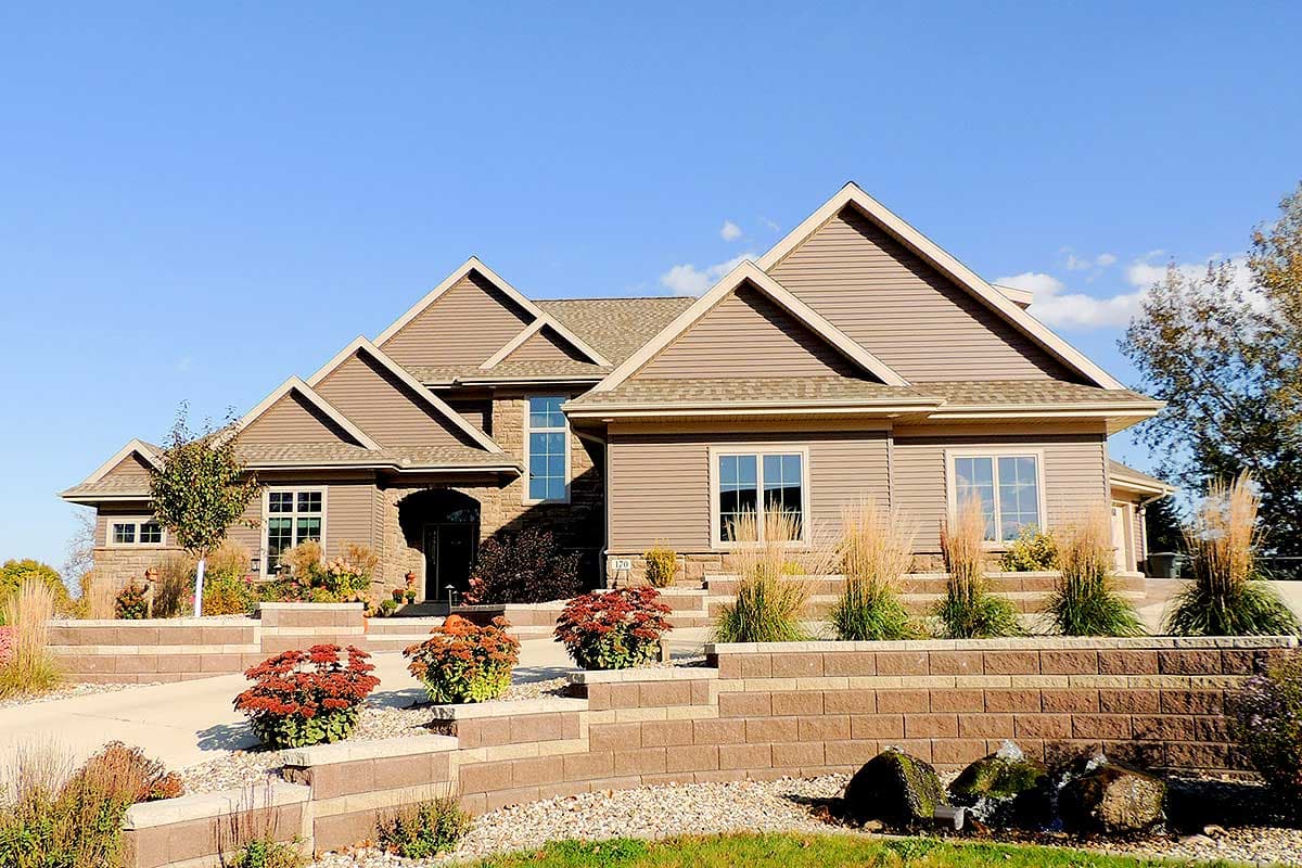 House plan exterior with multiple gables, stone accents, and a tiered landscape entry. Two-story home with a neutral siding color.