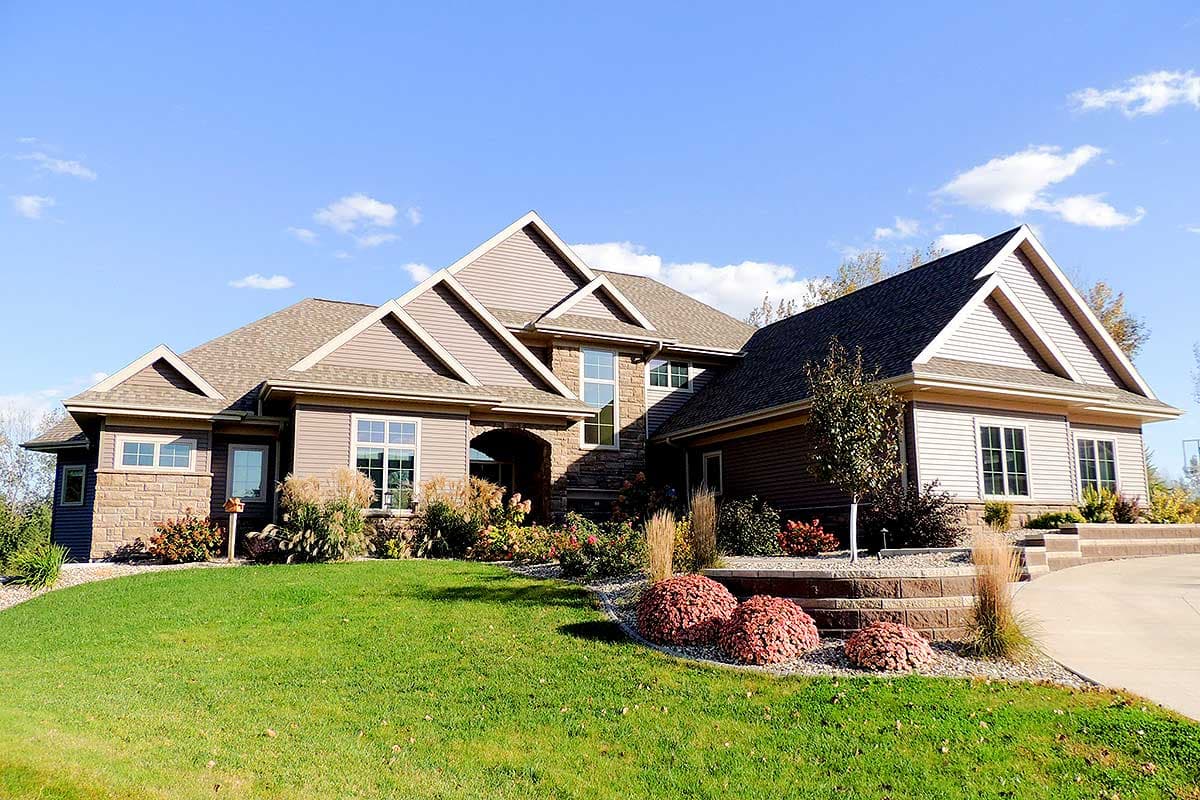 House plan exterior: Two-story residence with layered gables, stone accents, and a prominent arched entryway.