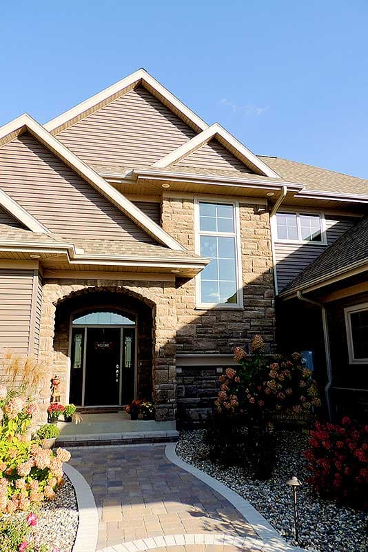 House plan exterior featuring stone facade, arched entryway with glass doors, prominent gables, and large vertical window.