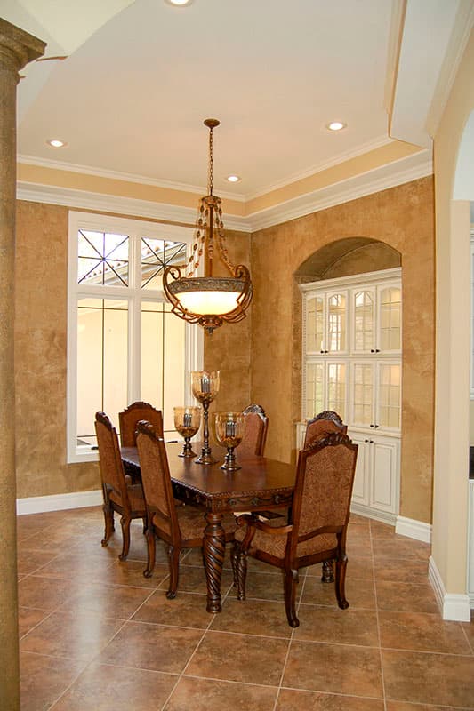 Dining room with ornate chandelier, six upholstered chairs around a carved wood table, and built-in cabinetry.
