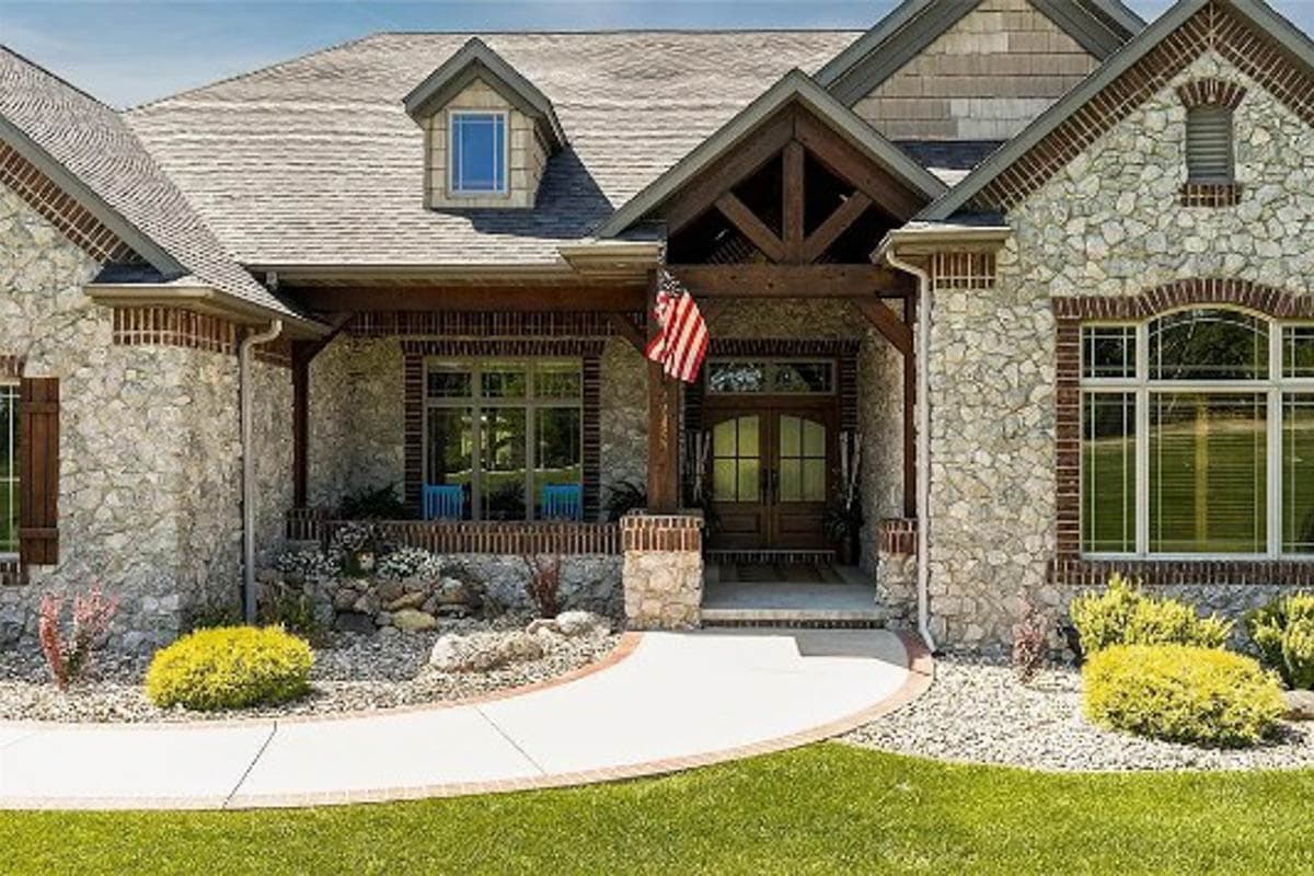 House plan exterior: Stone and brick facade with a covered front porch, exposed timber beams, dormer, and double front doors.