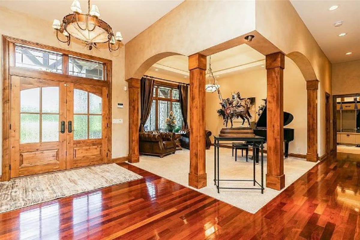 Interior view of a grand foyer with arched openings, wood columns, double wooden doors, and a grand piano.