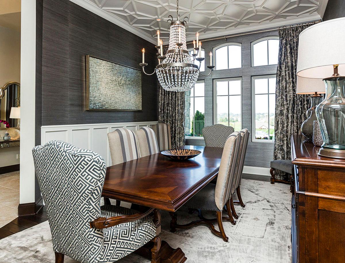 Dining room with coffered ceiling, dark grasscloth wallpaper, large dining table, and arched windows.