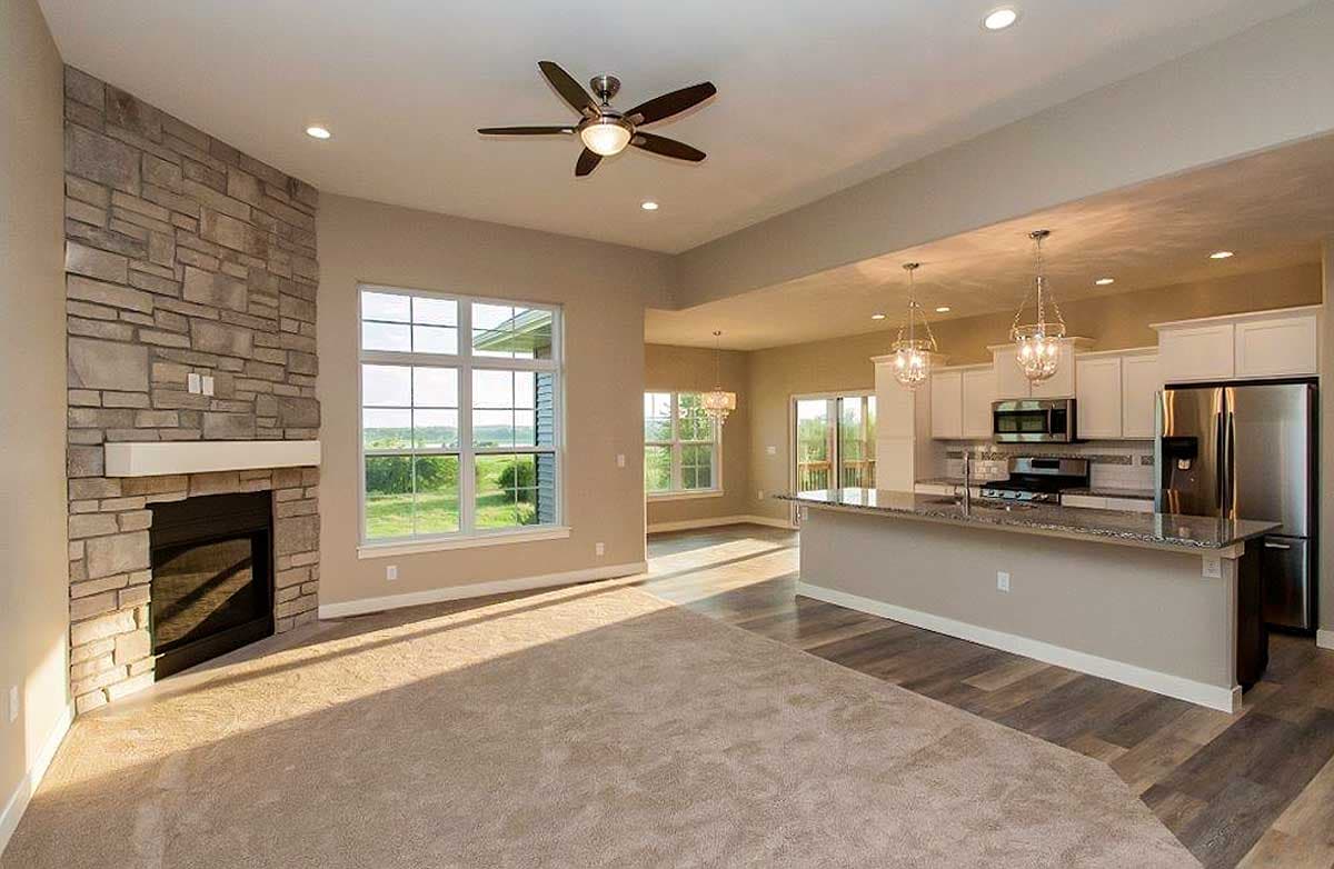 Interior view of open-concept living space with stone fireplace, large window, and kitchen island with pendant lighting.