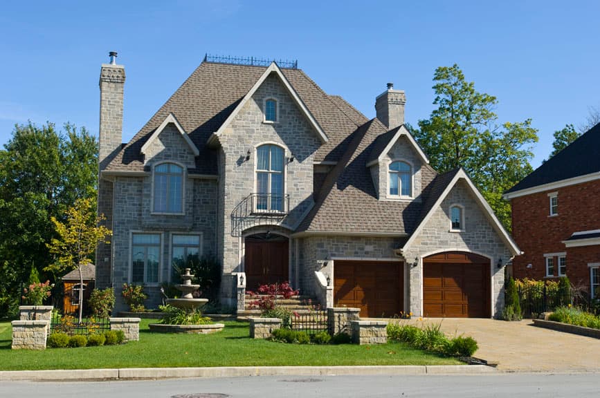 Two-story stone house plan exterior with gables, dormers, arched windows, balcony, and double garage.