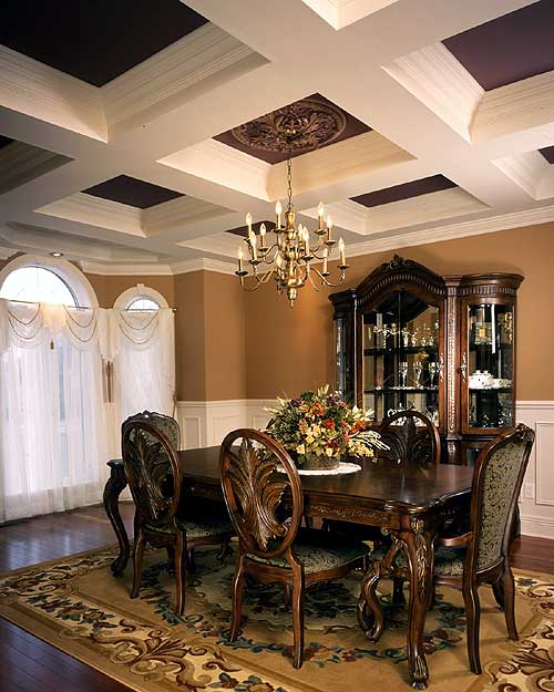 Dining room with coffered ceiling, ornate chandelier, traditional dining set, glass display cabinet, and arched windows with drapes.