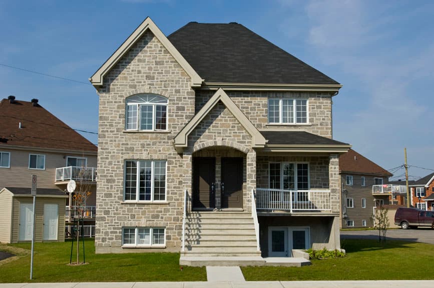 Two-story house plan exterior with stone facade, arched double entry, prominent gables, and multiple window configurations.