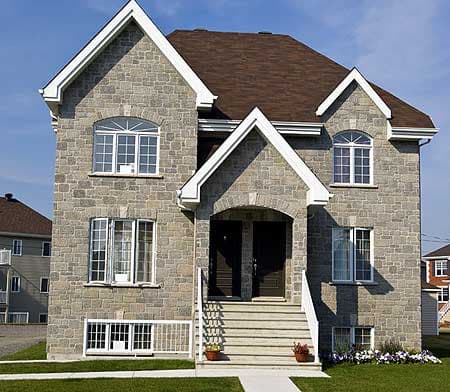 House plan exterior: stone facade, two stories, central arched entry with dual doors, prominent gables, and a multi-window facade.