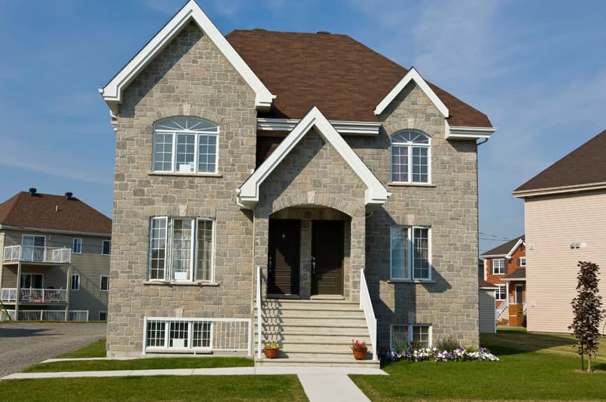 House plan exterior of two-story stone-clad duplex with arched entryways, symmetrical gables, and a brown asphalt shingle roof.
