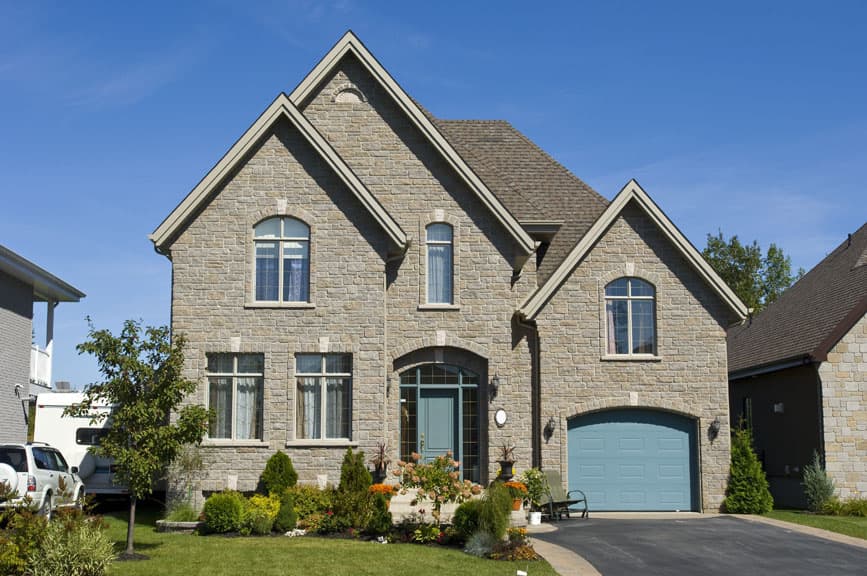 Two-story house plan exterior with stone facade, arched entry, gables, and attached garage.