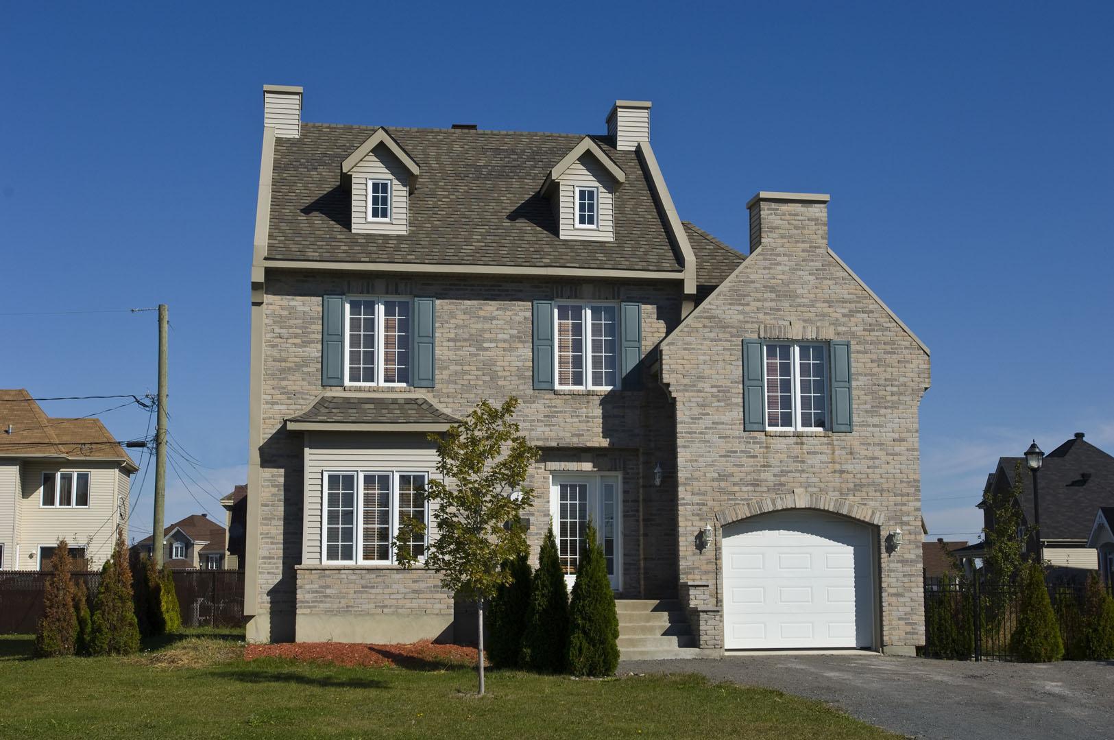 House plan exterior: Two-story brick home with dormers, shutters, central entrance, and attached garage with arched opening.
