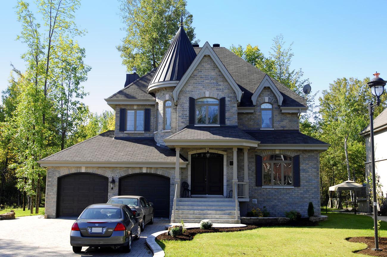 House plan exterior of a two-story stone home with a prominent conical turret, dual garage doors, and covered entry porch.