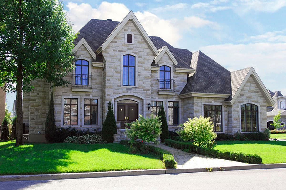 House plan exterior: stone facade, two-story, arched windows, multiple gables, and balconies.