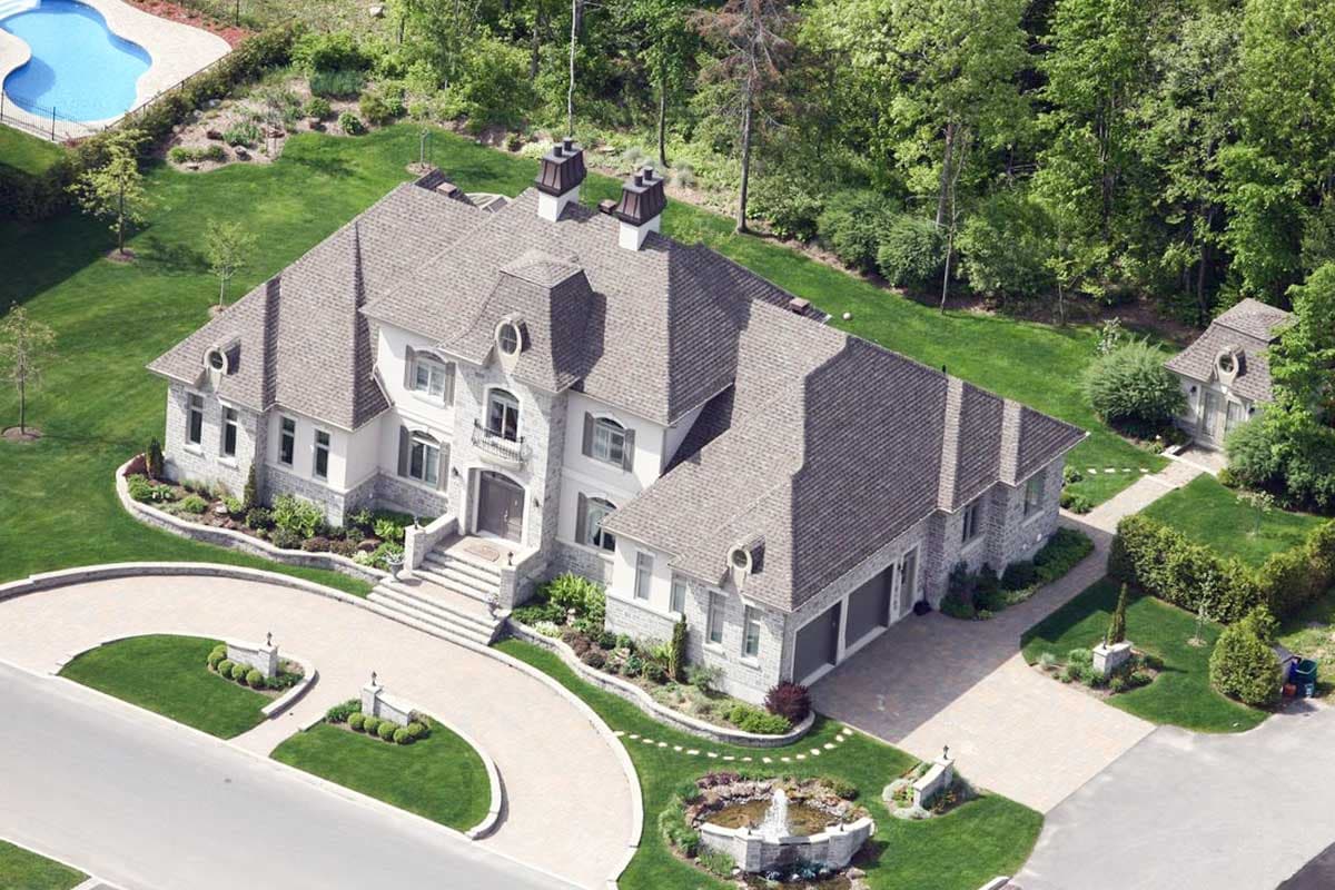 House plan exterior, multi-story residence with mansard roof, stone facade, multiple gables, and attached three-car garage.
