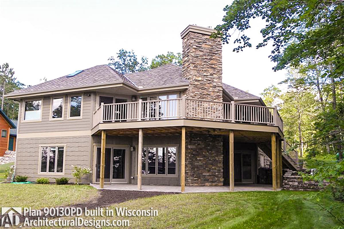 House plan exterior showing two stories, wraparound deck, and prominent stone chimney.
