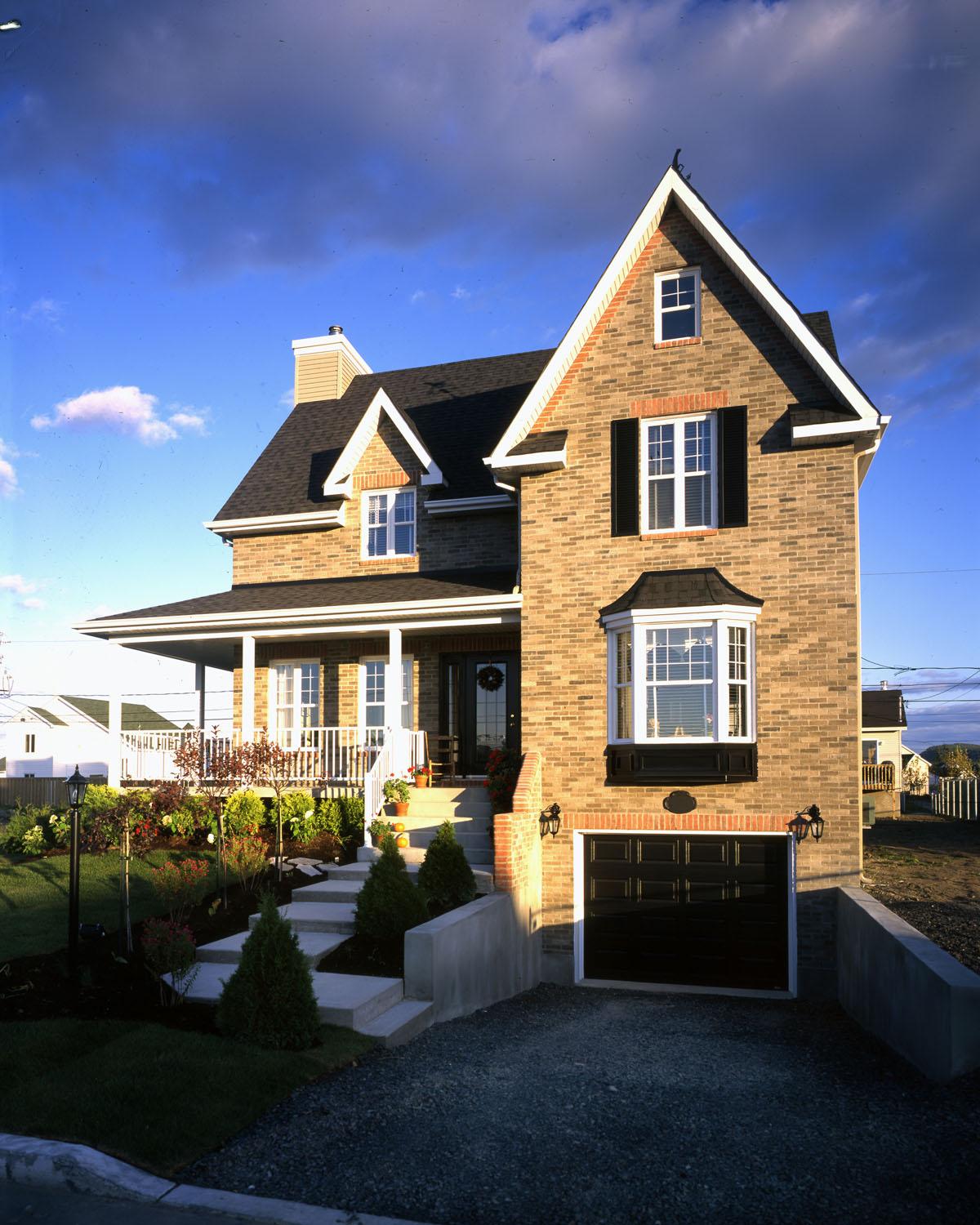 House plan exterior: Two-story brick home with a covered porch, dormers, bay window, and attached garage.