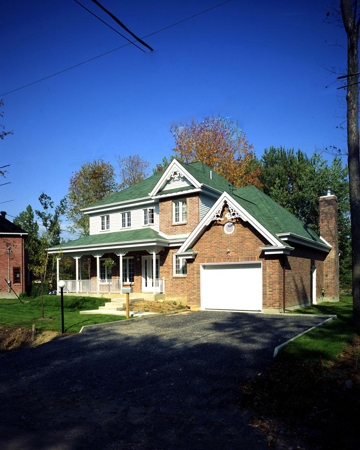 House plan exterior featuring a two-story brick home with a wraparound porch, green gables, and attached two-car garage.