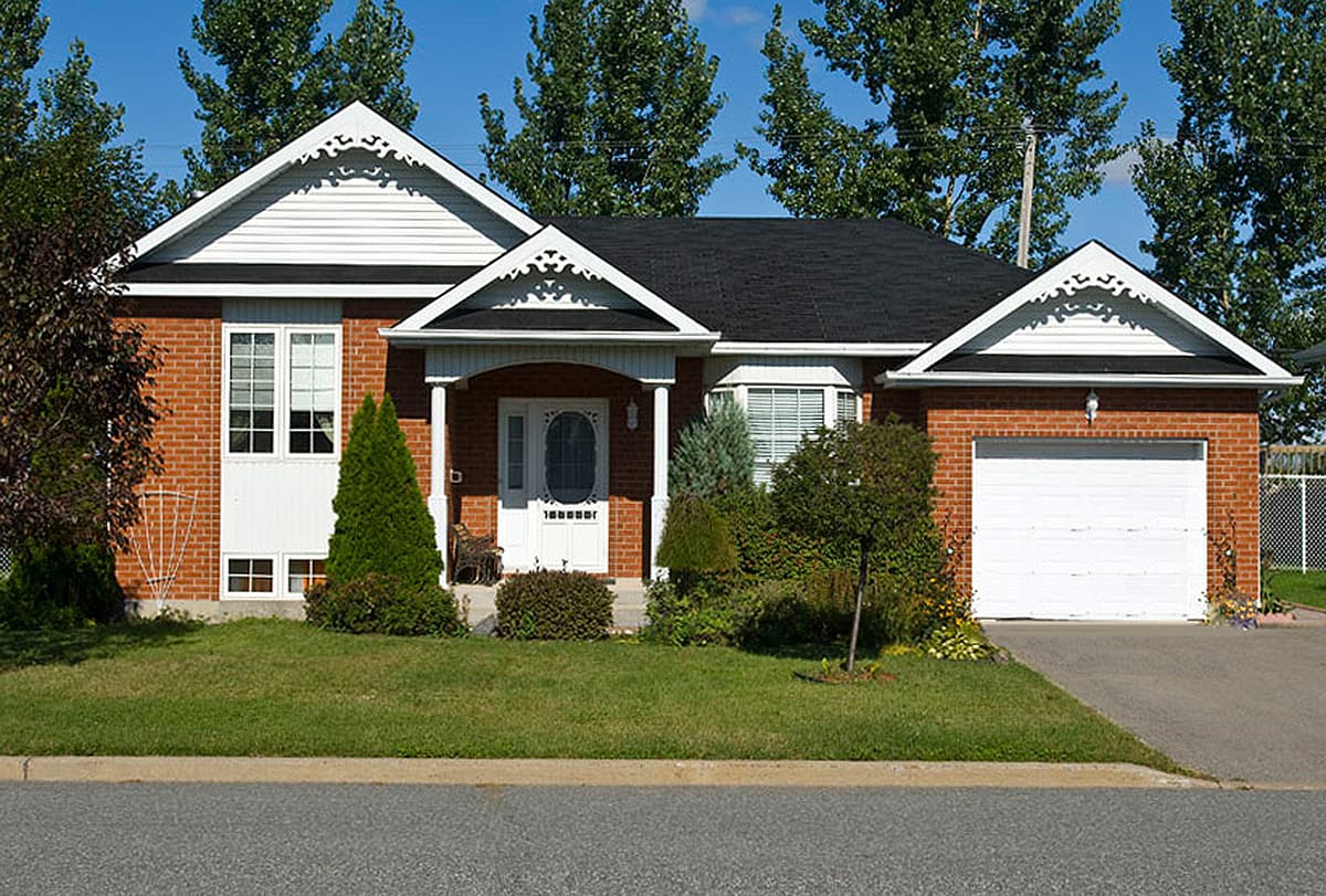House plan exterior: Red brick one-story home with a covered front porch, white gables with decorative trim, and an attached garage.