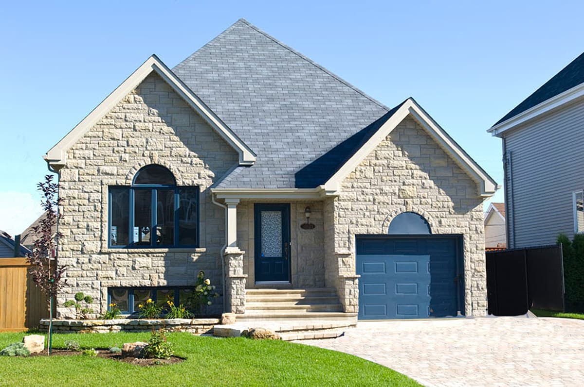 House plan exterior with stone facade, gabled roof, arched windows, covered entryway, and attached garage.