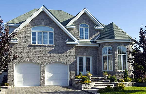 House plan exterior: Two-story home with stone facade, arched double garage, multiple gables, and bay windows.