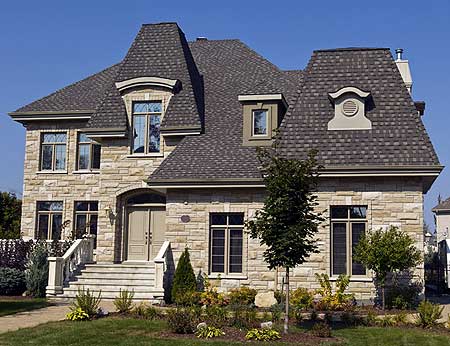 House plan exterior: stone facade, prominent Mansard rooflines, dormer windows, arched entryway, and a central staircase with stone balustrades.