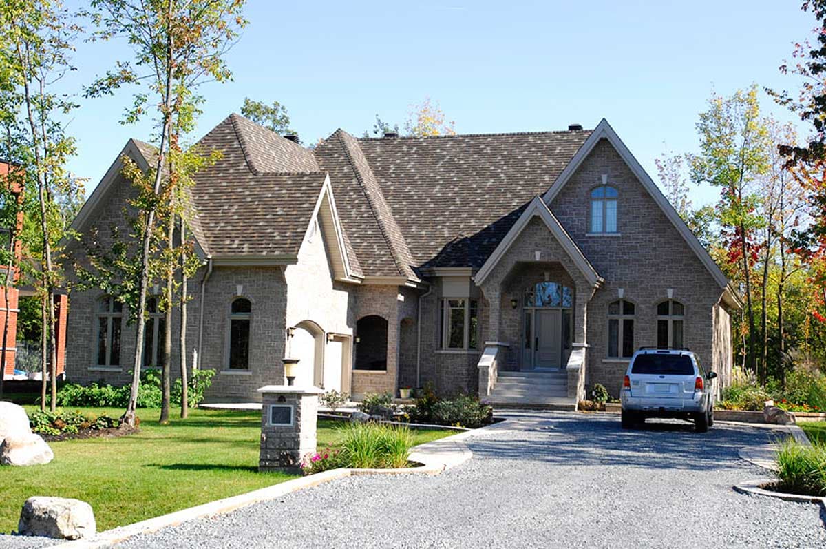House plan exterior with stone facade, prominent gables, arched entryway, and attached garage.