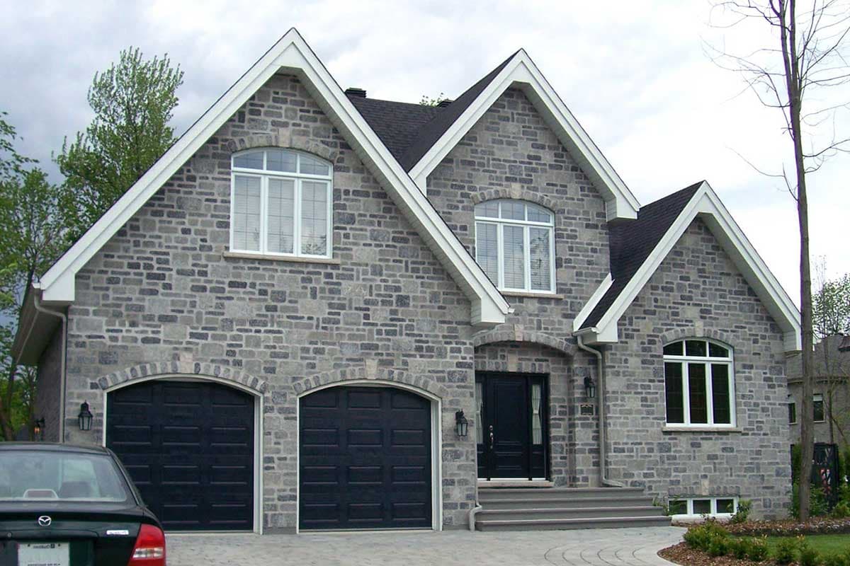 House plan exterior: Two-story home with stone facade, dual garage doors, arched entry, and prominent gables.