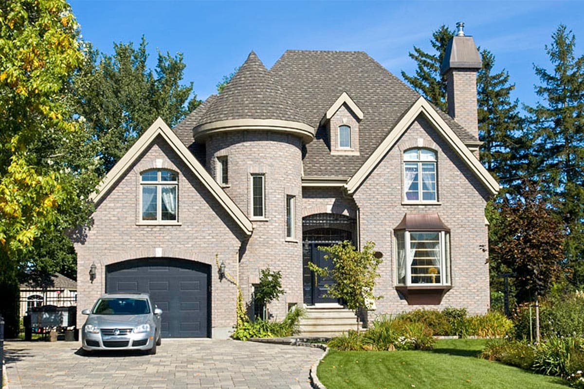 House plan exterior with a brick facade, gabled dormers, a turretted tower, and an attached garage.