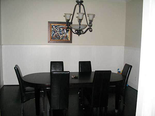 Dining room with oval table, six chairs, wainscoting, and a traditional chandelier.