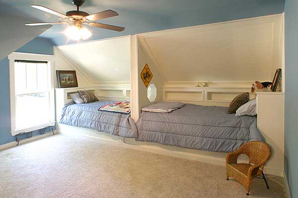 Built-in twin beds flank a central partition with shelving in this attic room. A ceiling fan is visible overhead.