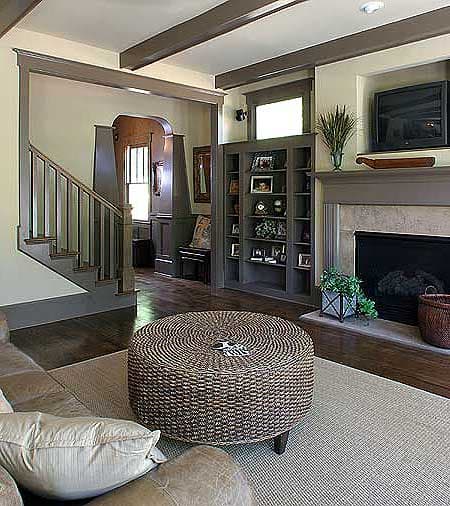 Interior view of a living room with a fireplace, built-in bookcase, staircase, and beamed ceiling.