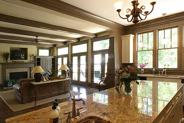 Open concept living space with beamed ceiling, fireplace, large windows, and kitchen island with granite countertop.