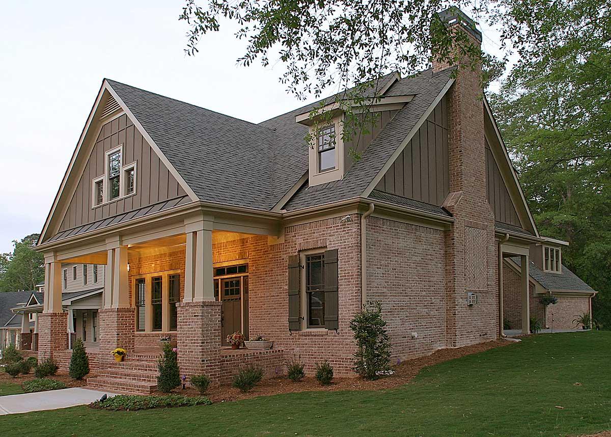 House plan exterior with brick facade, large covered porch supported by square columns, gabled dormer, and prominent brick chimney.